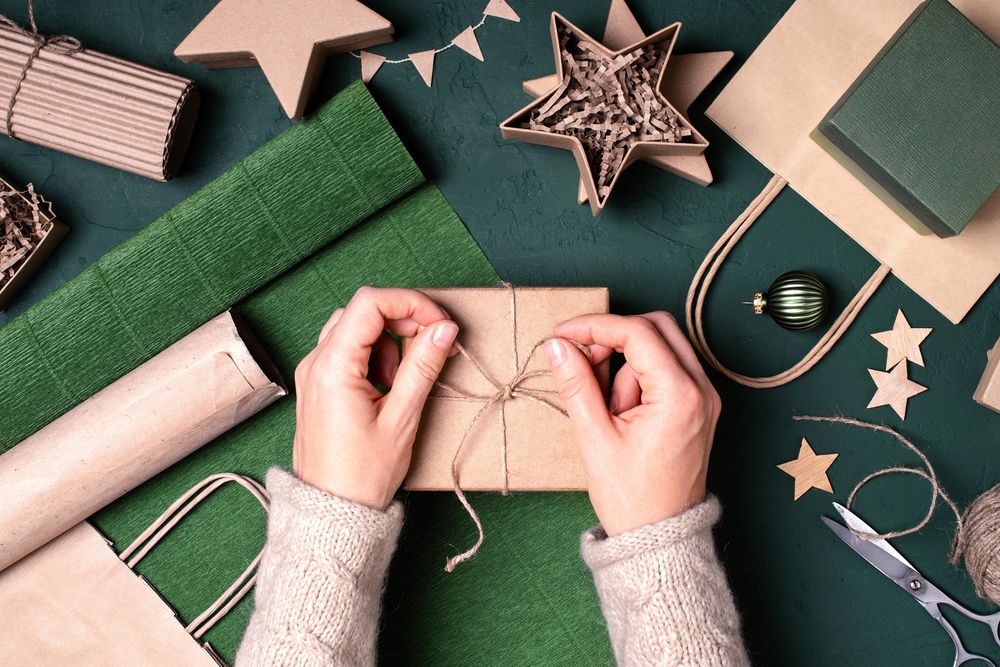 Woman’s hands tying twine on winter gift box with festive wrapping items around