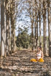 Calm adult pregnant woman practicing yoga while sitting in pose lotus on ground in park during sunny day