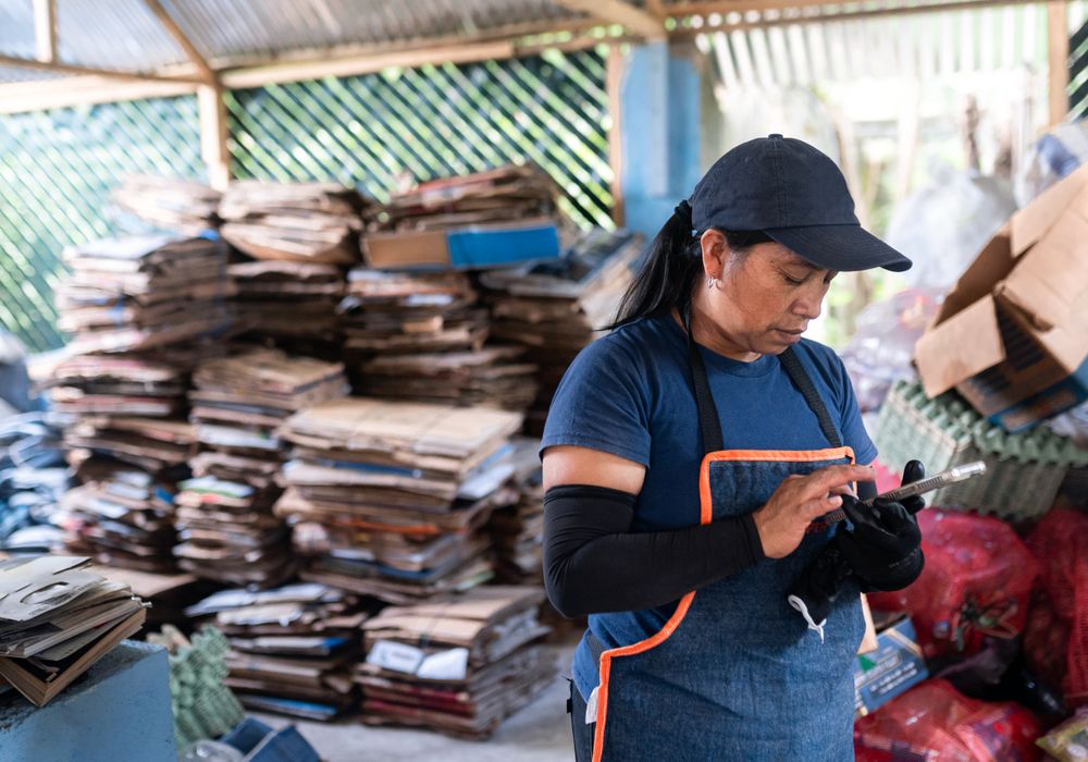 Hispanic Woman Writting Down Cardboard Stacking Records on Phone in a Recycling Plant