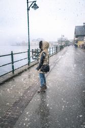 Woman under snowfall in Austrian town by a lake dressed in winter clothes