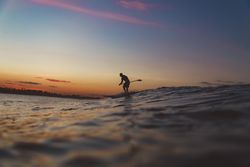 Man with paddle on surf board between waving water at sunset