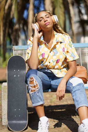 Female in bold patterned shirt sitting on park bench listening to something on large headphones