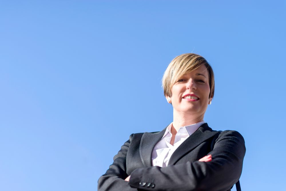 Happy proud businesswoman standing with arms crossed against blue sky