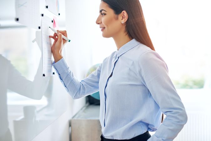 Confident female entrepreneur writing on a dry erase board in bright office