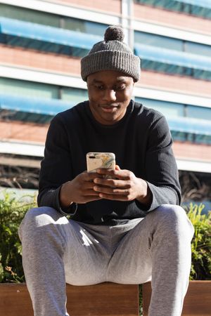 Serious Black man using smartphone sitting on street