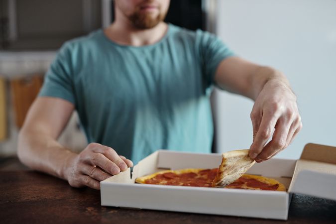 Cropped image of a man in blue shirt holding a slice of pepperoni pizza