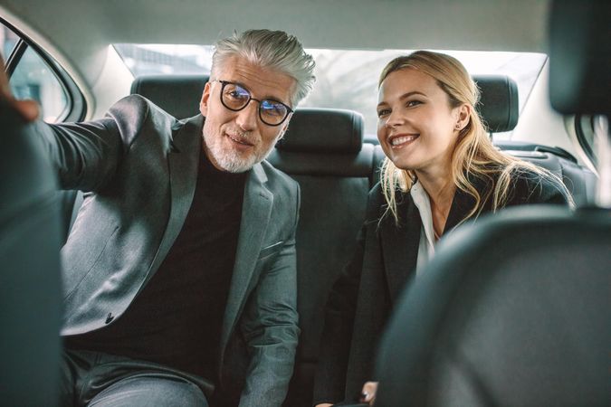 Business colleagues sitting in backseat of car and looking away smiling