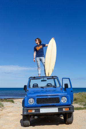 Man with surfboard standing on roof of car