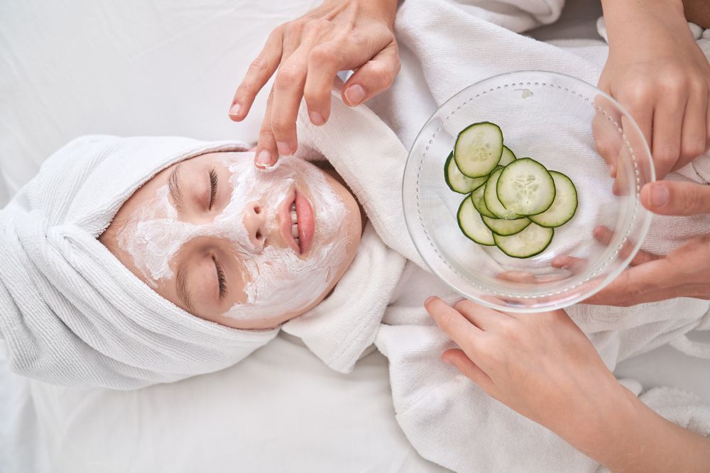 Unrecognizable woman putting cream mask with cucumber slices on