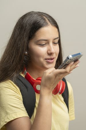 Teenage girl with red headphones speaking on smartphone voice assistant in casual portrait