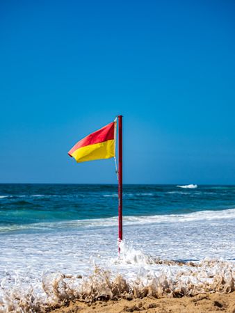 A restrictive flag is stuck in the sand on a beach on the ocean.