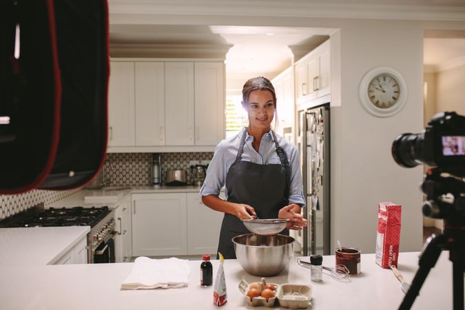 Woman preparing cake in kitchen and recording video on camera