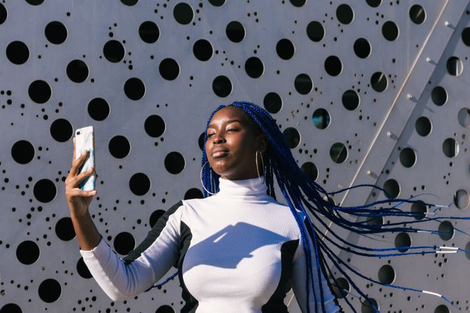 Serious Black woman taking selfie on street