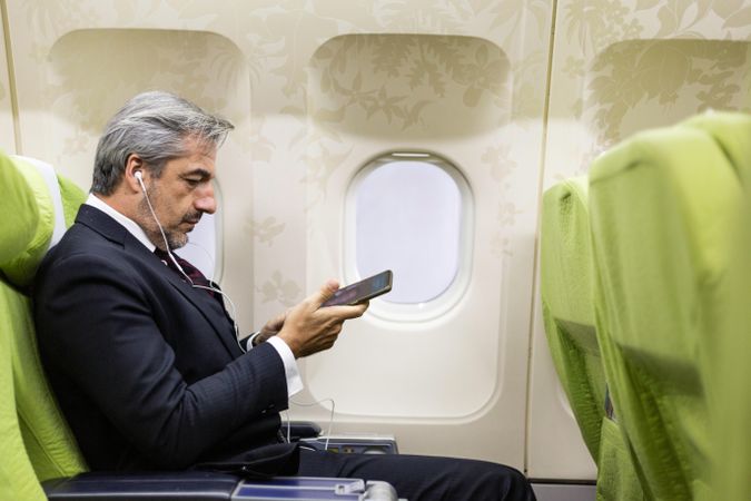 Side view of man listening to music through earphones in airplane cabin