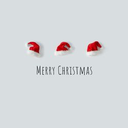 Santa hats in a row on light background above “Merry Christmas”