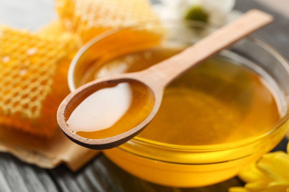 Flowers, glass bowl with honey and dipper on wooden background, closeup