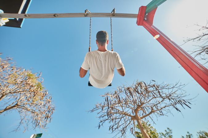 Man swinging on playground in sunlight