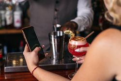 Customer having a cocktail in a traditional cocktail bar while using the smartphone
