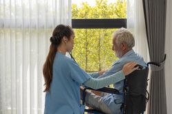 Female medical professional examining chest of older male in wheel chair