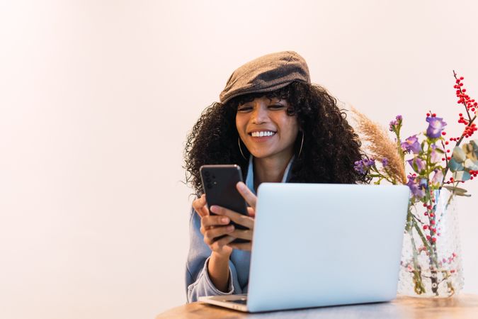 Cheerful Black woman using smartphone and laptop