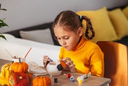 A little girl paints a clay hand made pumpkin. Halloween party. Crafts for children.