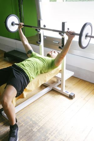 Man in green t-shirt lifting heavy bar exercising chest