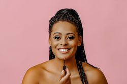 Happy Black woman applying lip gloss and looking at camera