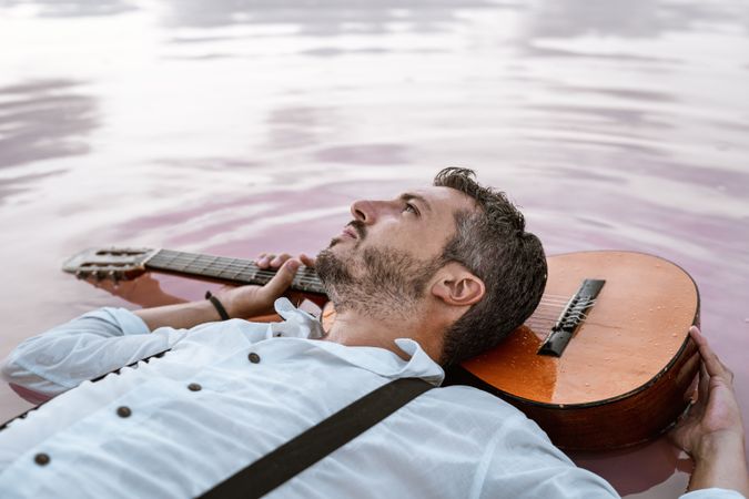 Man resting in water with guitar at seaside