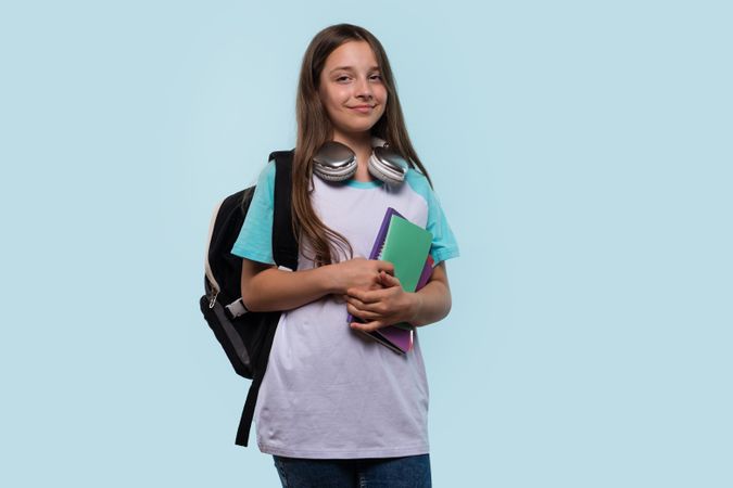 Teen girl with backpack and headphones holding notebooks