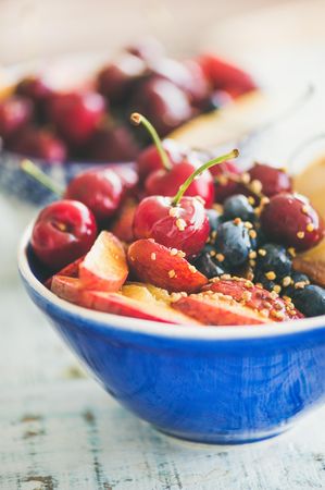 Close up of blue bowl of fresh fruit with cherries, peaches, blueberry, vertical composition