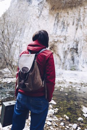 Woman with case jumping on rocks above stream