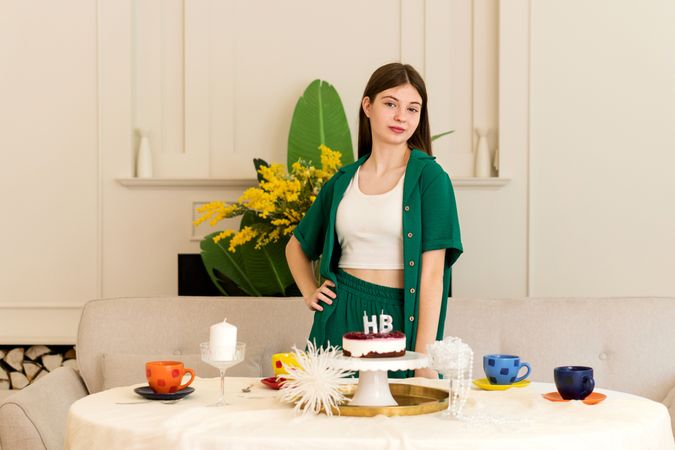 Girl in green outfit stands confidently behind table