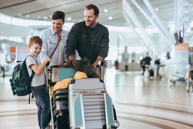 Couple looking at their son at airport with luggage trolley