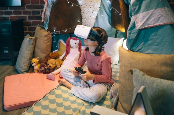 Little girl using virtual reality glasses to study science sitting over mat in tent