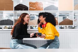 Positive multiethnic female friends using smartphones and laughing in cafe