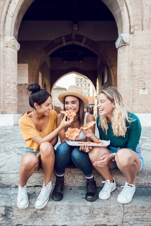 Happy diverse friends eating pizza on stairs in Italy