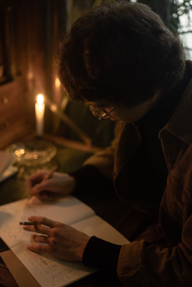 Person writing in a notebook and holding cigarette