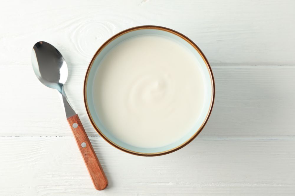 Bowl of sour cream yogurt with spoon on plain background