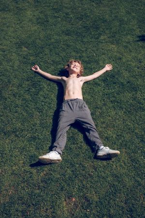 Content boy with hands and legs apart on lawn