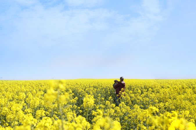Rear view of woman holding her baby in yellow field