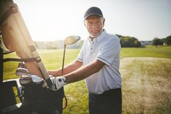 Man standing at golf cart with clubs