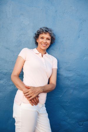 Portrait of relaxed mature lady leaning to a blue wall