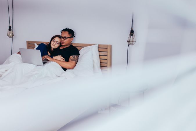 Multiracial couple relaxing in bedroom with laptop