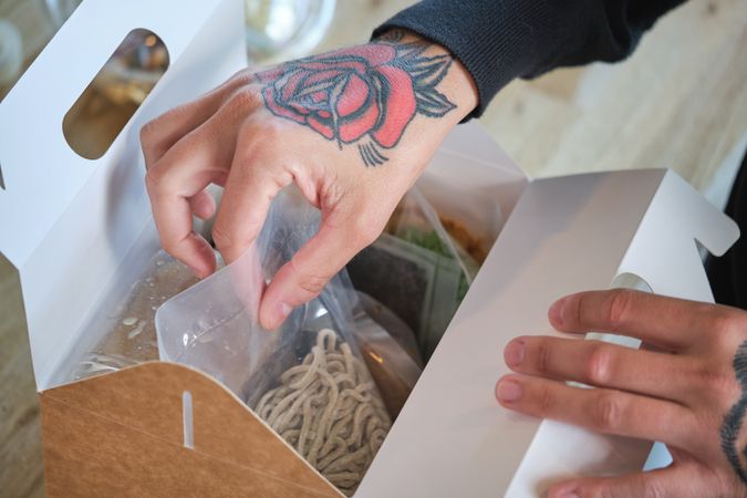 Unrecognizable cook putting ingredients for ramen in container