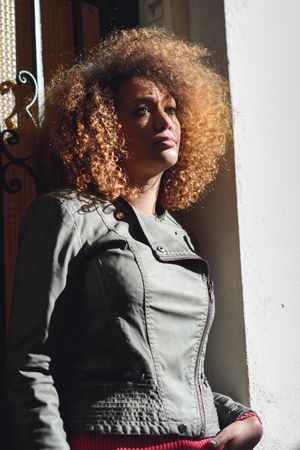 Woman with curly hair and green jacket pictured in door frame on sunny day
