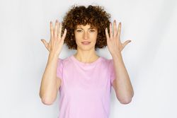 Female in light pink t-shirt standing with hands up with palms facing inwards in blank space