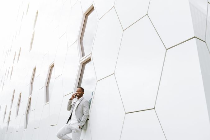Elegant Black man talking smartphone leaning on geometrical wall