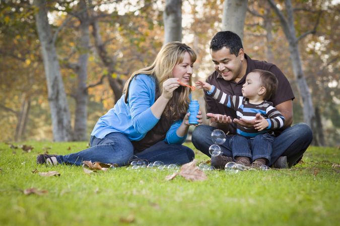 Family of Three Playing with Bubbles In The Park