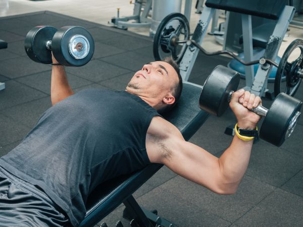 Strong man exercising with dumbbells on bench