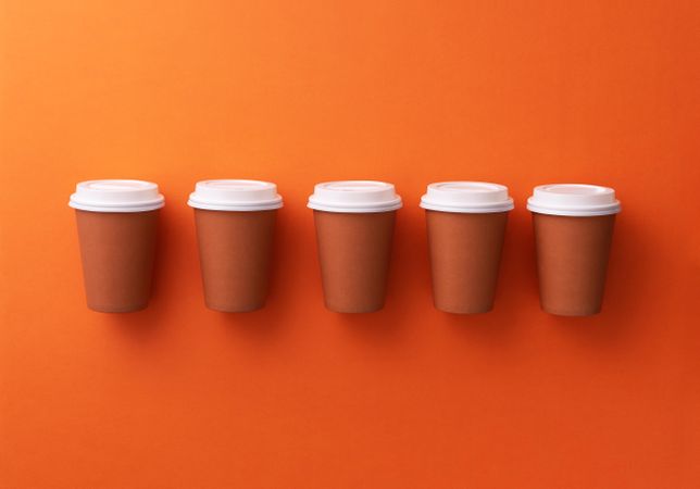 Single row of disposable coffee cups on orange background